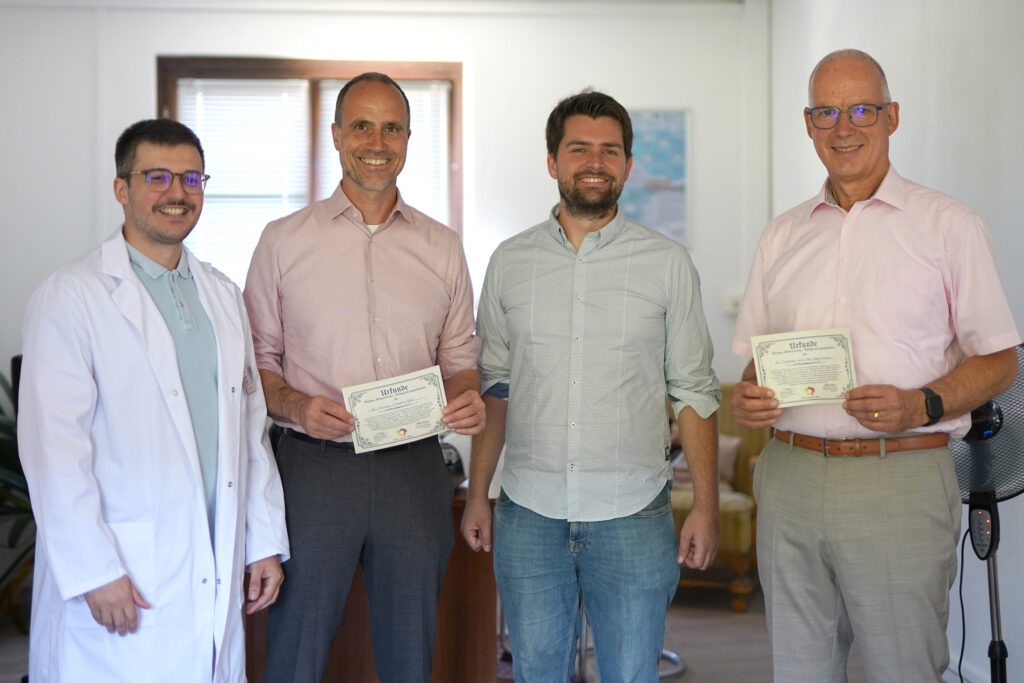 Nachdem Wissenschaftsminister Clemens Hoch (2.v.l.) und JGU-Präsident Prof. Dr. Georg Krausch (r.) den Escape Room auf dem Gutenberg-Campus erfolgreich absolviert haben, erhalten sie vom Projektteam des BNE Escape Game Lab, Fabian Schäfer (l.) und Timo Graffe (2.v.r.), eine Urkunde. (Foto/©: Tobias Rosenbaum / Zukunft@JGU)