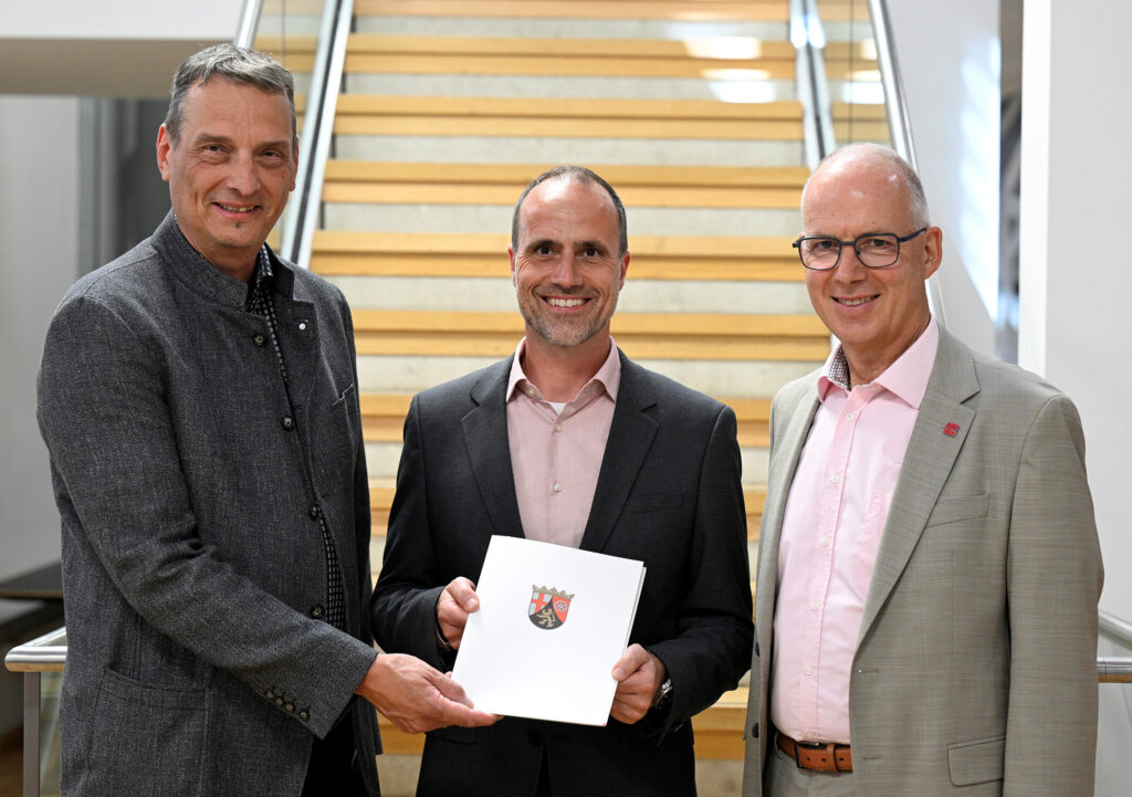 Wissenschaftsminister Clemens Hoch (Mitte) überreicht den Förderbescheid zum Ausbau der Nutzung des Mainzer Zyklotrons an JGU-Präsident Prof. Dr. Georg Krausch (r.) und Prof. Dr. Stefan Müller-Stach (l.), JGU-Vizepräsident für Forschung und wissenschaftliche Karrierewege. (Foto: Peter Pulkowski)